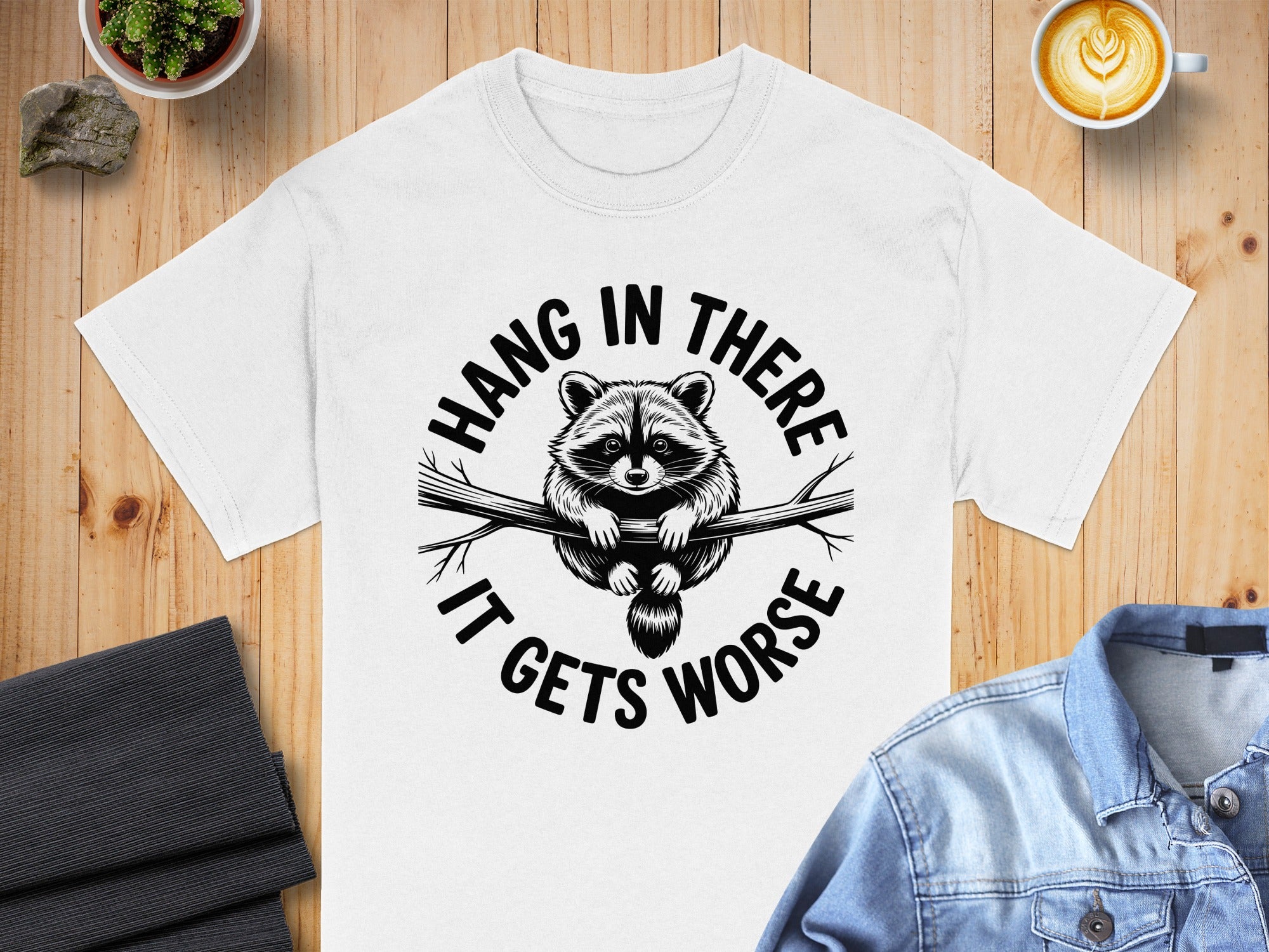 White t-shirt with a raccoon illustration and "Hang in there, it gets worse" text.